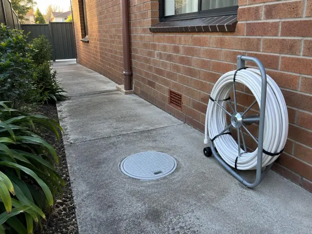Capped round access cover set in a concrete side path beside a brick house in Seaforth