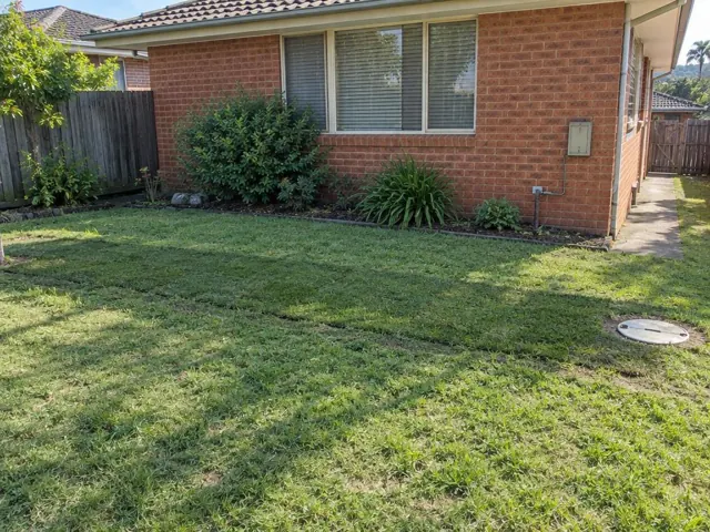 Backfilled trench across a lawn beside a brick house with a round sewer cover in Seaforth